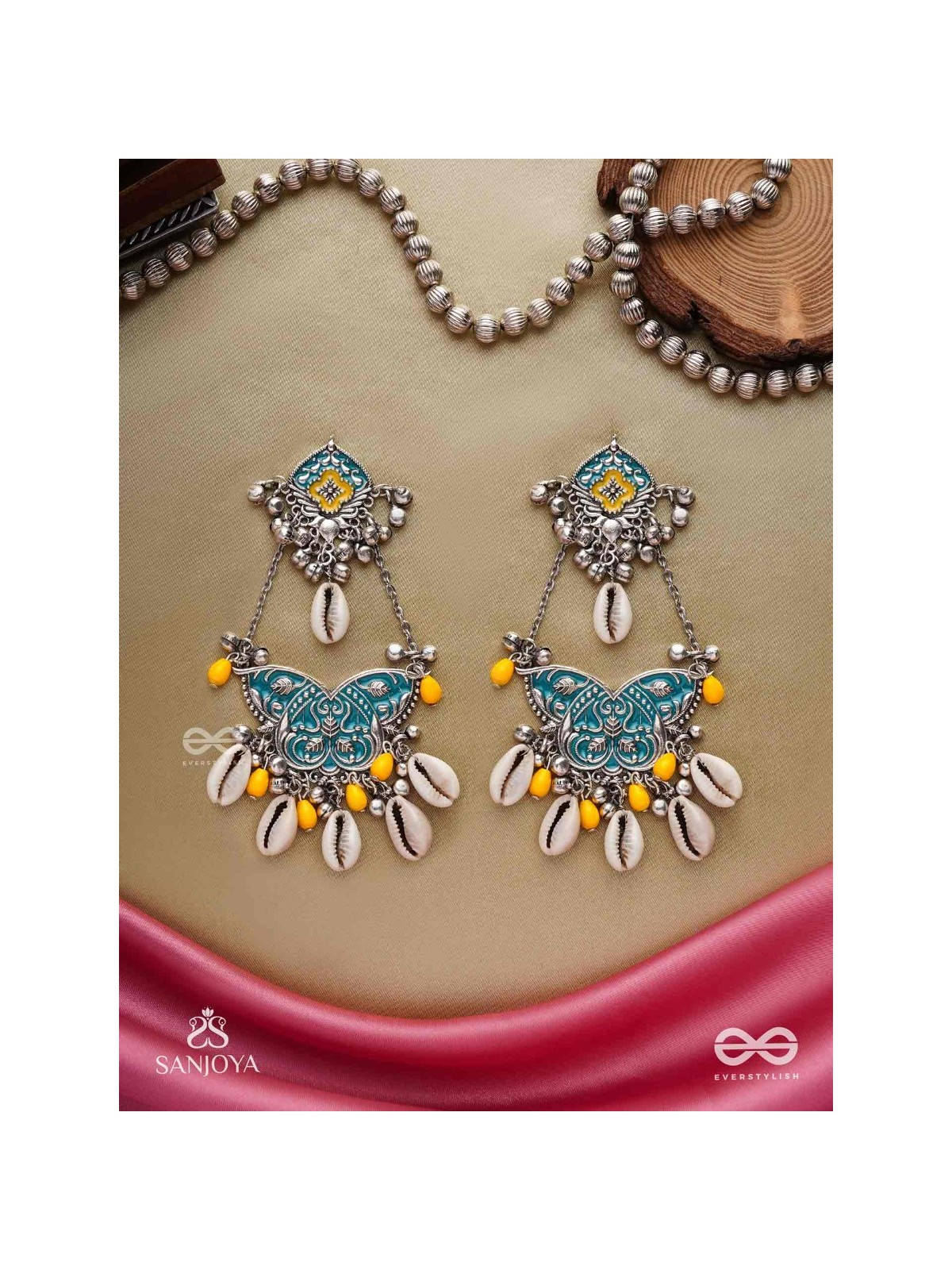 SHANKHA PUSHPA- CONCH BLOSSOM-OXIDIZED EARRINGS WITH PASTEL-HUED METALWORK, EMBELLISHED WITH DELICATE COWRIE SHELLS, YELLOW BEADS AND GHUNGROO