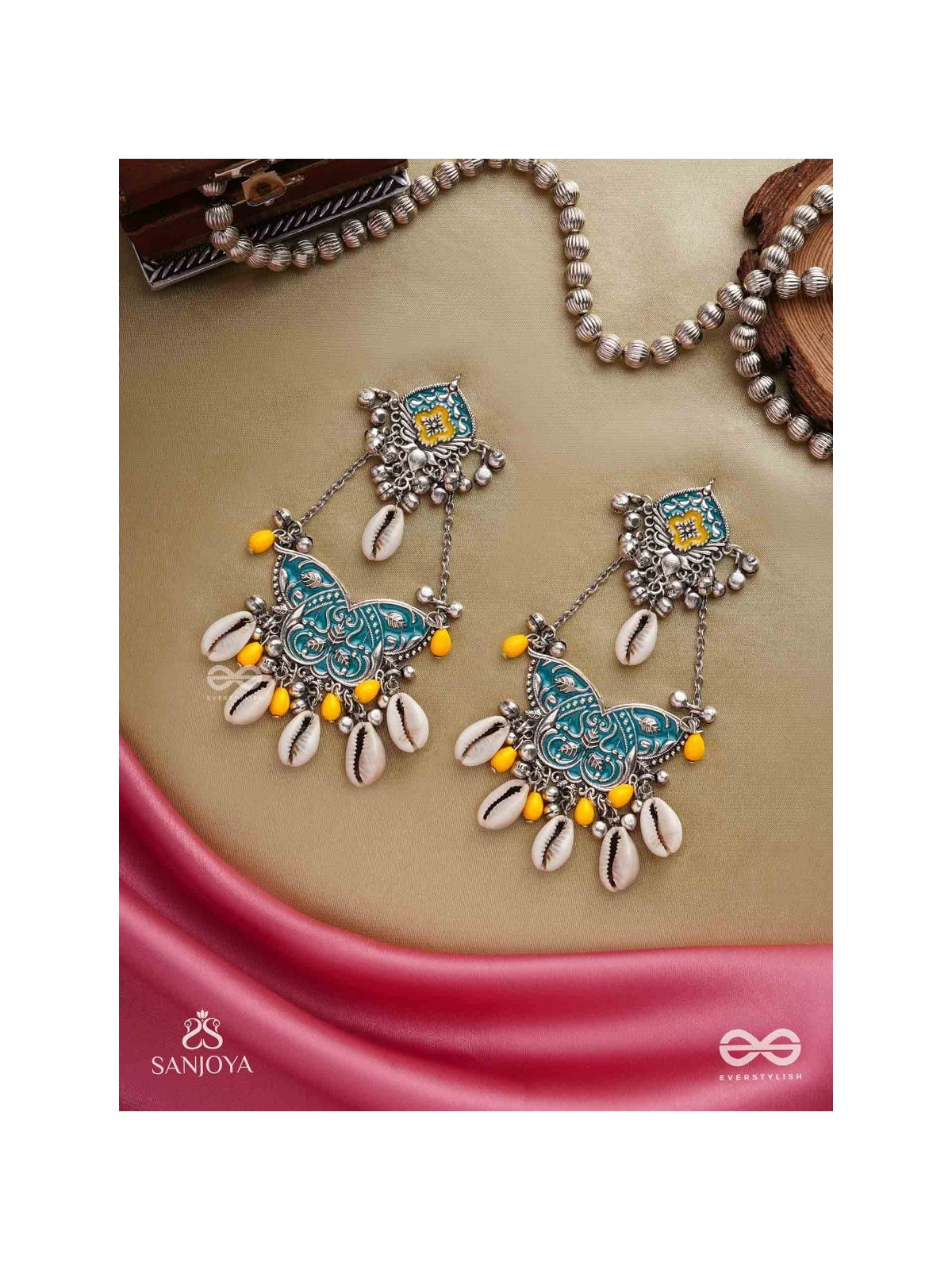 SHANKHA PUSHPA- CONCH BLOSSOM-OXIDIZED EARRINGS WITH PASTEL-HUED METALWORK, EMBELLISHED WITH DELICATE COWRIE SHELLS, YELLOW BEADS AND GHUNGROO