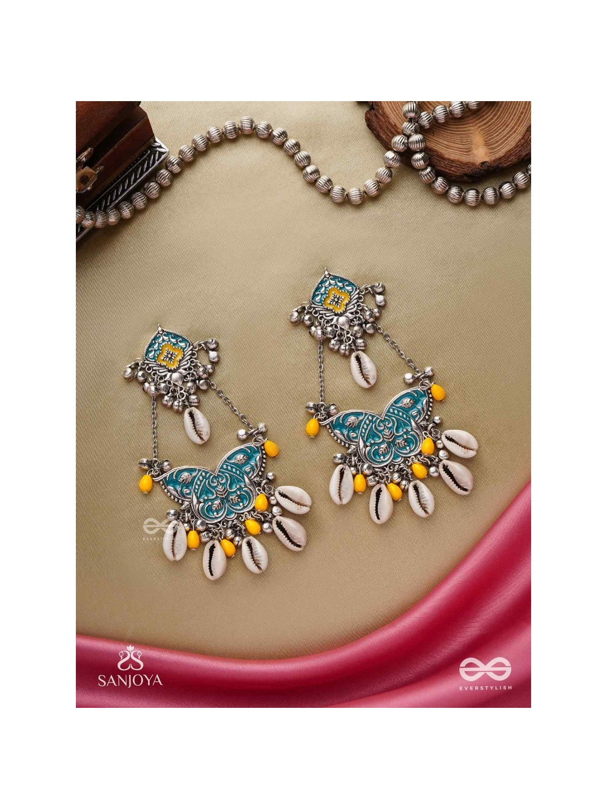 SHANKHA PUSHPA- CONCH BLOSSOM-OXIDIZED EARRINGS WITH PASTEL-HUED METALWORK, EMBELLISHED WITH DELICATE COWRIE SHELLS, YELLOW BEADS AND GHUNGROO