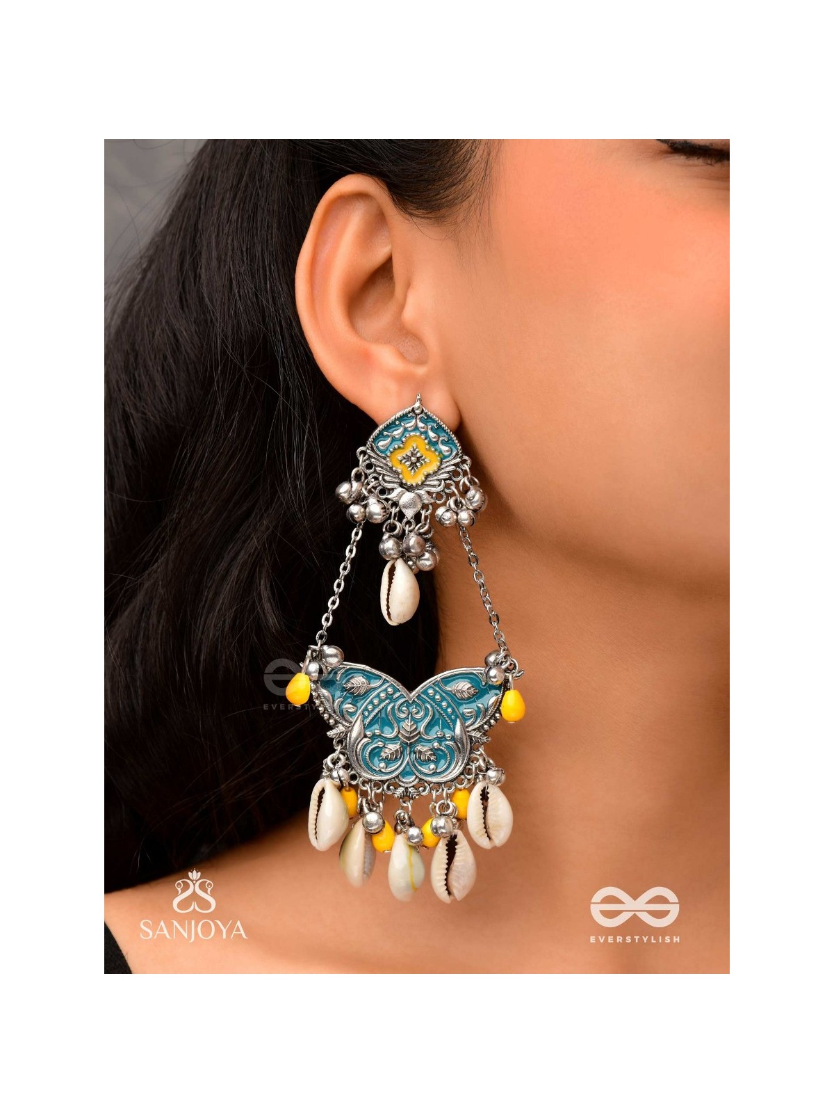 SHANKHA PUSHPA- CONCH BLOSSOM-OXIDIZED EARRINGS WITH PASTEL-HUED METALWORK, EMBELLISHED WITH DELICATE COWRIE SHELLS, YELLOW BEADS AND GHUNGROO