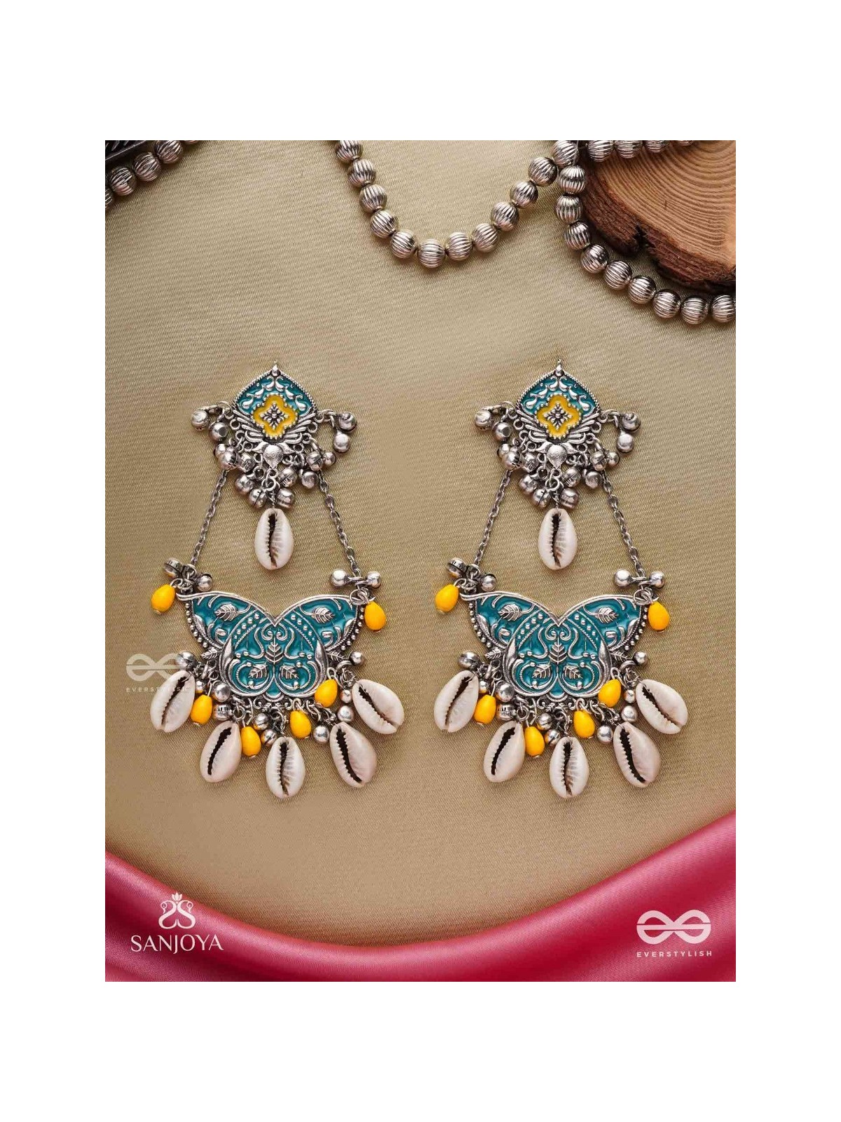 SHANKHA PUSHPA- CONCH BLOSSOM-OXIDIZED EARRINGS WITH PASTEL-HUED METALWORK, EMBELLISHED WITH DELICATE COWRIE SHELLS, YELLOW BEADS AND GHUNGROO